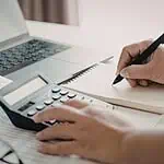 person writing and using a calculator