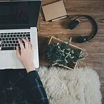 Person typing on a laptop with various tech accessories on a wooden desk.