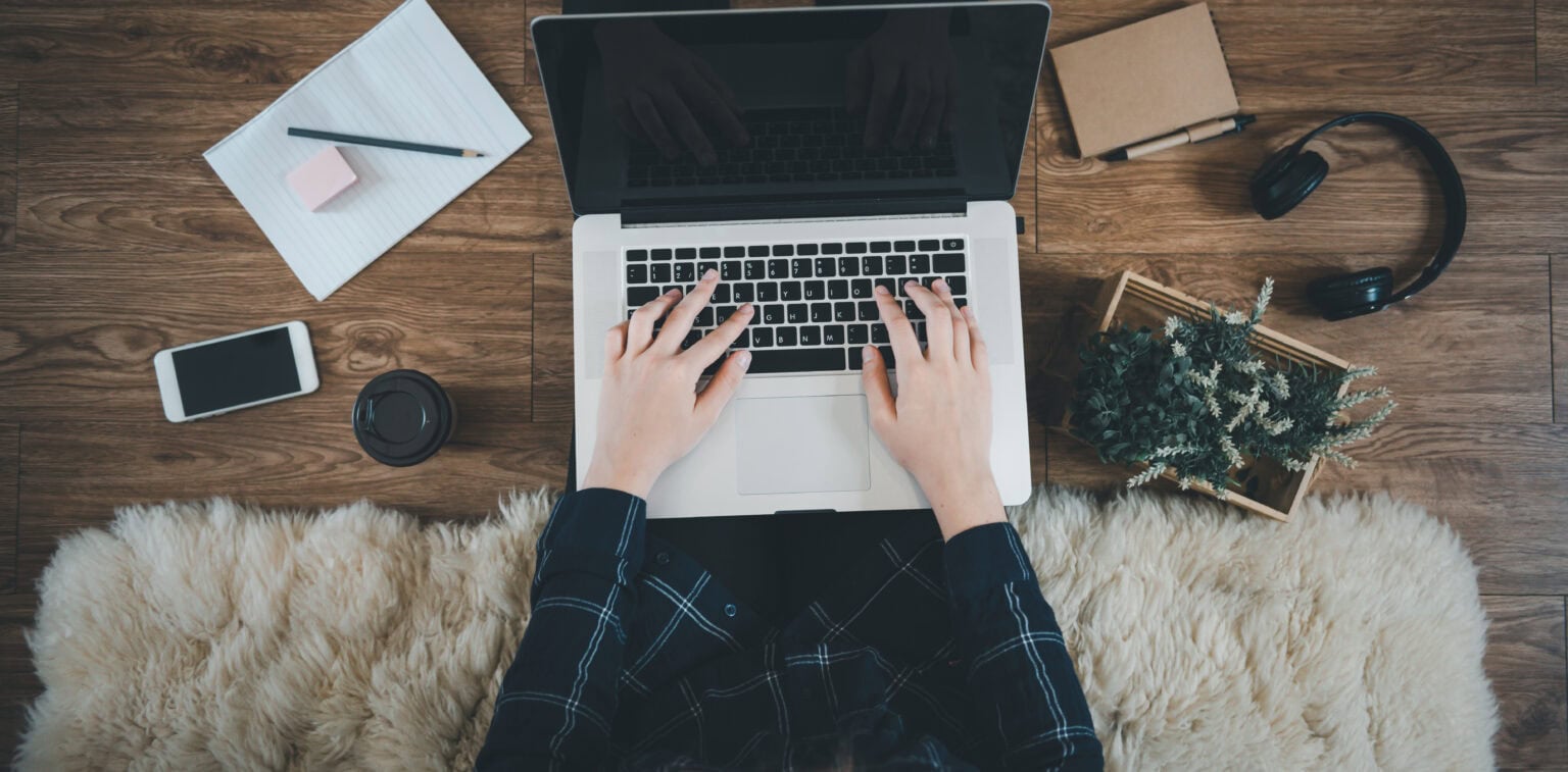 Person typing on a laptop with various tech accessories on a wooden desk.